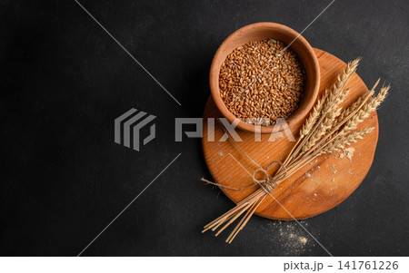 Wheat grains and wheat ears on wooden board over dark background with copy space 141761226