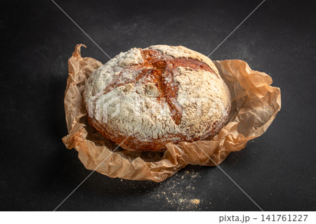 Fresh artisan sourdough bread loaf on baking paper over dark background Fresh artisan sourdough bread loaf on baking paper over dark background 141761227