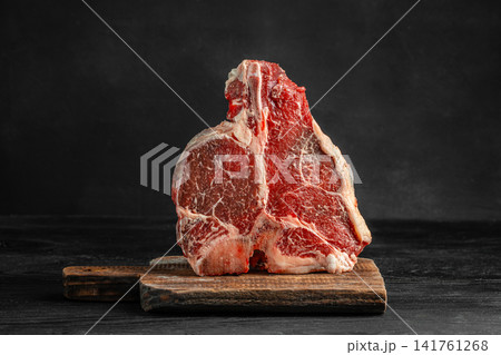 Raw porterhouse steak on wooden cutting board over dark background Raw porterhouse steak on wooden cutting board over dark background 141761268