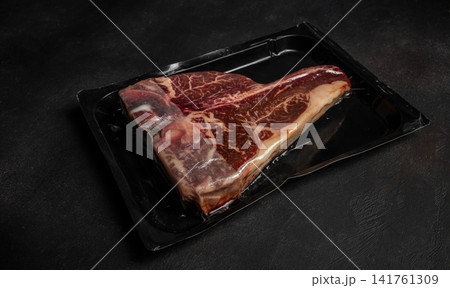 Vacuum packed raw beef steak in black tray on dark background 141761309