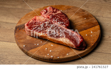 Raw bone in beef steak with coarse sea salt on wooden board Raw bone in beef steak with coarse sea salt on wooden board 141761327