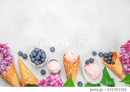 Strawberry ice cream in waffle cones with blueberries and lilac flowers, summer dessert background Strawberry ice cream in waffle cones with blueberries and lilac flowers, summer dessert background 141761382