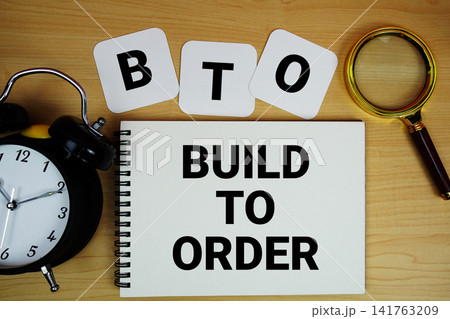 BTO Build to Order text written on notepad with magnifying glass and alarm clock on wooden background 141763209
