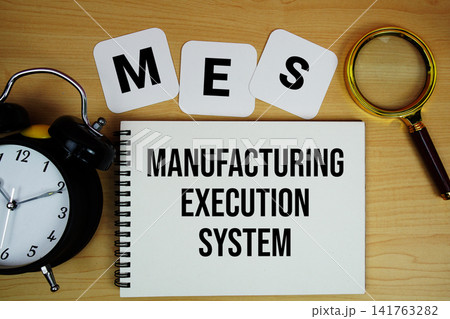 MES Manufacturing Execution System text written on notepad with magnifying glass and alarm clock on wooden background 141763282