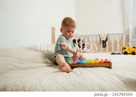 Two year old boy playing xylophone at home. Tapping colorful keys develops fine motor skills and musical ear. Early childhood education through rhythm and sound exploration Two year old boy playing xylophone at home. Tapping colorful keys develops fine motor skills and musical ear. Early childhood education through rhythm and sound exploration 141765504