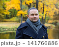 Stylish man in navy coat and scarf walking in autumn park near river 141766886