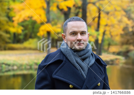 Stylish man in navy coat and scarf walking in autumn park near river Stylish man in navy coat and scarf walking in autumn park near river 141766886