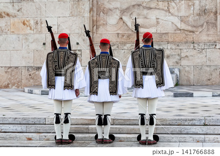 Traditional Evzones guards standing in ceremonial uniform in Athens, Greece. Iconic symbol of Greek history, heritage and national identity near the Hellenic Parliament. Traditional Evzones guards standing in ceremonial uniform in Athens, Greece. Iconic symbol of Greek history, heritage and national identity near the Hellenic Parliament. 141766888