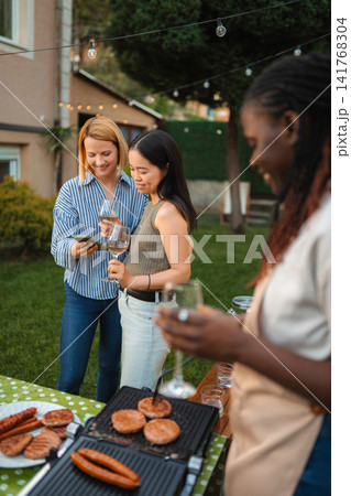 Diverse women friends enjoying backyard barbecue and using smartphone Diverse women friends enjoying backyard barbecue and using smartphone 141768304
