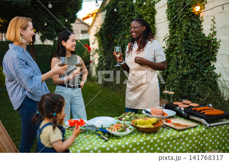 Diverse friends enjoying backyard barbecue party with food and drinks Diverse friends enjoying backyard barbecue party with food and drinks 141768317