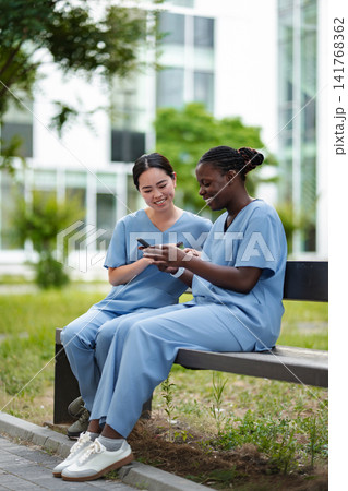 Diverse nurses taking a break on bench using smart phones 141768362