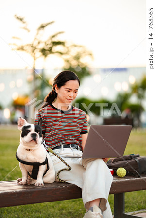 Japanese woman remote working with her French bulldog in park Japanese woman remote working with her French bulldog in park 141768365