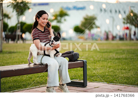 Japanese woman calling embracing French bulldog in park Japanese woman calling embracing French bulldog in park 141768366