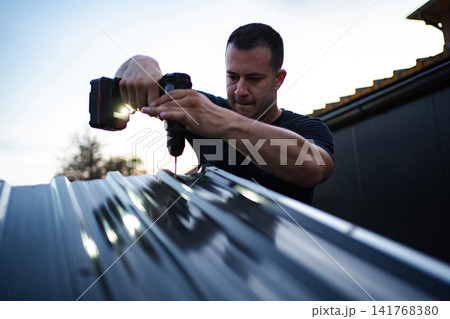 Handyman drilling metal roof during home improvement project Handyman drilling metal roof during home improvement project 141768380