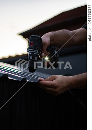 Worker using cordless drill on corrugated metal roof Worker using cordless drill on corrugated metal roof 141768382