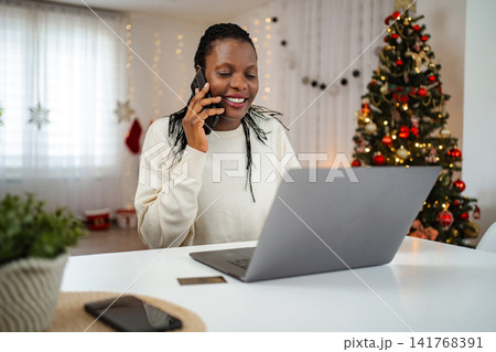 Woman making phone call while holiday shopping online with laptop 141768391