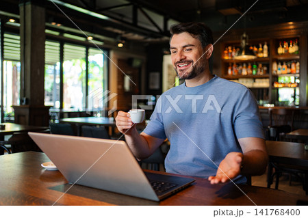 Man drinking coffee working on laptop in cafe Man drinking coffee working on laptop in cafe 141768400