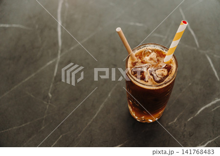 Top-down view of a layered iced espresso with orange juice and paper straw. Refreshing specialty coffee served in a decorative glass 141768483