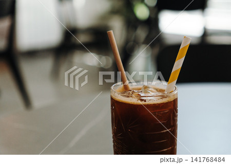 Refreshing iced espresso layered with orange juice served with a paper straw in a modern cafe. Cold specialty coffee beverage on a table Refreshing iced espresso layered with orange juice served with a paper straw in a modern cafe. Cold specialty coffee beverage on a table 141768484
