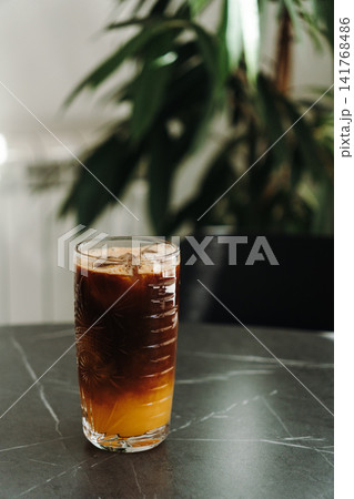 Layered iced espresso with orange juice served in a decorative glass on a cafe table. Refreshing specialty coffee beverage with natural light Layered iced espresso with orange juice served in a decorative glass on a cafe table. Refreshing specialty coffee beverage with natural light 141768486