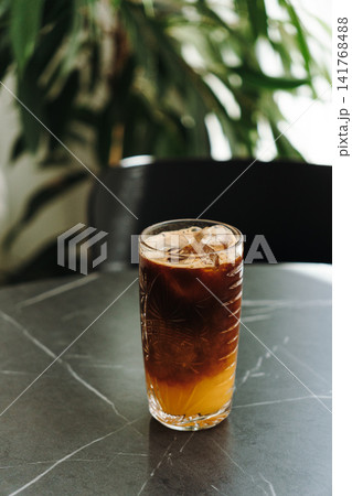 Layered iced espresso with orange juice served in a decorative glass on a cafe table. Refreshing specialty coffee beverage with natural light Layered iced espresso with orange juice served in a decorative glass on a cafe table. Refreshing specialty coffee beverage with natural light 141768488
