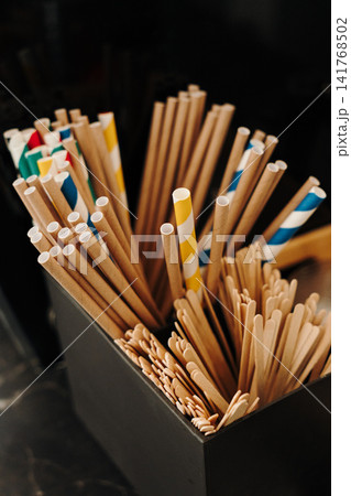 Paper drinking straws and wooden stirrers neatly organized on a coffee shop counter. Eco-friendly accessories for serving beverages Paper drinking straws and wooden stirrers neatly organized on a coffee shop counter. Eco-friendly accessories for serving beverages 141768502