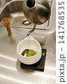 Hot water being poured over sifted matcha powder in a ceramic bowl on a digital scale. Traditional Japanese tea preparation in progress 141768535