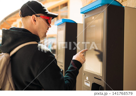 Young man using outdoor automated ticket machine or parking meter Young man using outdoor automated ticket machine or parking meter 141768579