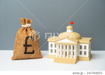 A government building and a British pound money bag. State budget. Project funding. Social spending. Tax collection and budget replenishment. A government building and a British pound money bag. State budget. Project funding. Social spending. Tax collection and budget replenishment. 141768855