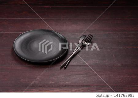 An empty round ceramic plate on a dark, textured brown background. An empty round plate An empty round ceramic plate on a dark, textured brown background. An empty round plate 141768983