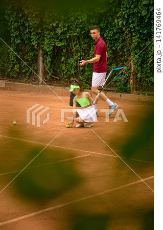 Young girl practices running footwork with male tennis coach during clay court drill Young girl practices running footwork with male tennis coach during clay court drill 141769464