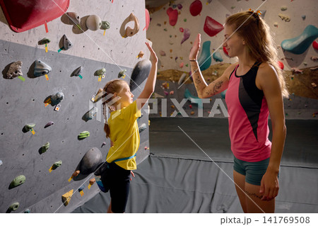 Young girl giving high five to female climbing coach after indoor training exercise Young girl giving high five to female climbing coach after indoor training exercise 141769508
