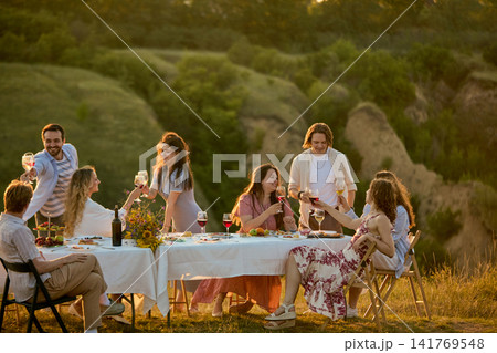 Diverse friends enjoying welcoming countryside meal around elegant white table Diverse friends enjoying welcoming countryside meal around elegant white table 141769548
