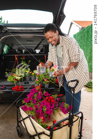 Happy woman loading new spring flowers into car trunk Happy woman loading new spring flowers into car trunk 141769709