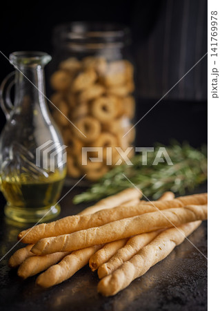 Golden Breadsticks With Olive Oil and Rosemary on Dark Table for Rustic Italian Snack Golden Breadsticks With Olive Oil and Rosemary on Dark Table for Rustic Italian Snack 141769978