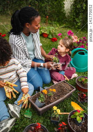 Mother teaching children planting flowers in garden Mother teaching children planting flowers in garden 141770052