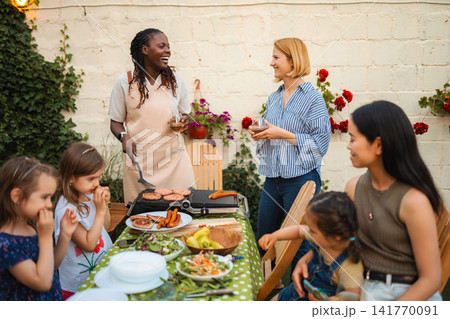 Diverse friends and children enjoying barbecue dinner party outdoors Diverse friends and children enjoying barbecue dinner party outdoors 141770091