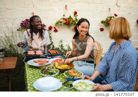 Multiethnic women friends enjoying backyard BBQ grilling and talking Multiethnic women friends enjoying backyard BBQ grilling and talking 141770107