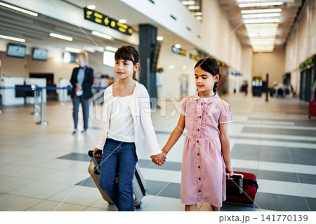 Children holding hands walking with luggage through airport terminal Children holding hands walking with luggage through airport terminal 141770139