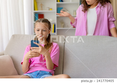 Young daughter focusing on smartphone while her mother gesturing with concern 141770405
