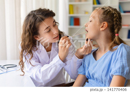 Female doctor supporting young girls chin and performing throat swab examination Female doctor supporting young girls chin and performing throat swab examination 141770406