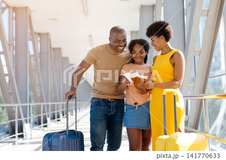Black family checking passports and boarding passes together in bright airport Black family checking passports and boarding passes together in bright airport 141770633