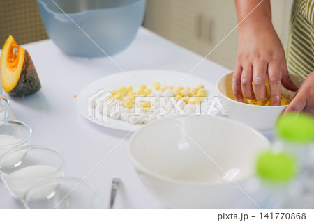 Housewife hands make dessert, cook food, mixing fresh ingredients with sugar in kitchen bowl, preparing vibrant pumpkin dough for small round dumplings, creating delicious traditional sweet treat Housewife hands make dessert, cook food, mixing fresh ingredients with sugar in kitchen bowl, preparing vibrant pumpkin dough for small round dumplings, creating delicious traditional sweet treat 141770868