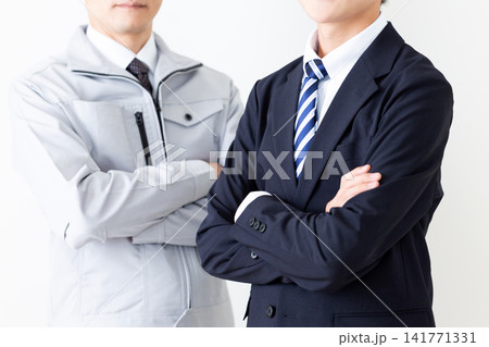 腕組みをするリクルートスーツを着た若い男性と作業服のミドル男性 腕組みをするリクルートスーツを着た若い男性と作業服のミドル男性 141771331