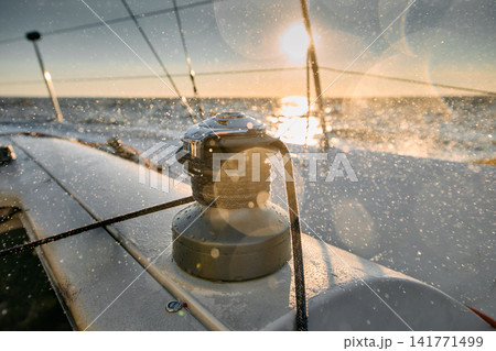 yacht winch with rope on a sailing boat with splashes of water at sunset, the side of a sailing boat, the rails of a sailing boat, the glare of the sun on the object, Sailing regatta yacht winch with rope on a sailing boat with splashes of water at sunset, the side of a sailing boat, the rails of a sailing boat, the glare of the sun on the object, Sailing regatta 141771499