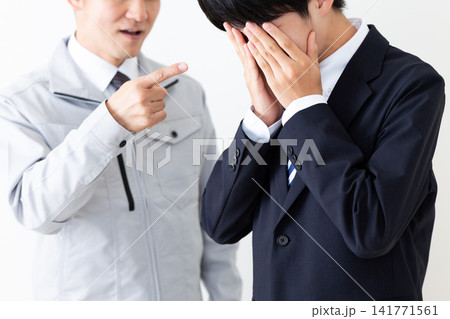 怒られて落ち込むリクルートスーツを着た若い男性と作業服のミドル男性 怒られて落ち込むリクルートスーツを着た若い男性と作業服のミドル男性 141771561