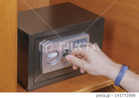 Man hand opens electronic safe box using emergency key overcome dead battery problem inside wooden cabinet shelf for secure personal item retrieval system Man hand opens electronic safe box using emergency key overcome dead battery problem inside wooden cabinet shelf for secure personal item retrieval system 141772006