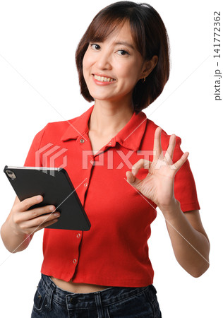 Asian woman holding tablet in red shirt smiling and making okay gesture, isolated portrait for communication, technology and business concept Asian woman holding tablet in red shirt smiling and making okay gesture, isolated portrait for communication, technology and business concept 141772362