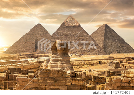 Famous Giza Pyramids stand behind the Great Sphinx under a dramatic sunset desert sky, Egypt. 141772405