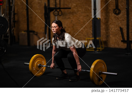 Woman preparing to lift barbell in gym for strength training Woman preparing to lift barbell in gym for strength training 141773457